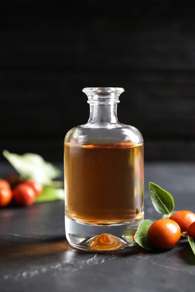 Glazen fles met jojoba olie en zaden op grijze stenen tafel tegen donkere achtergrond — Stockfoto