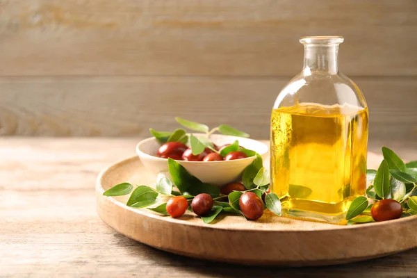 Glass bottle with jojoba oil and seeds on wooden table. Space for text — Stock Photo, Image