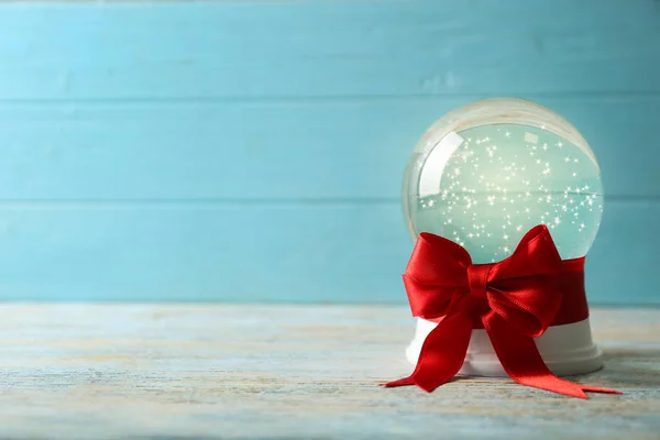 Bela bola de neve de Natal com arco vermelho na mesa de madeira branca contra fundo azul, espaço para texto — Fotografia de Stock