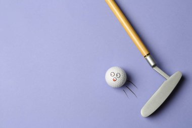 Eflatun arka planda kulüpten uçan komik yüzlü golf topu - yaratıcı görüntü. Üst görünüm
