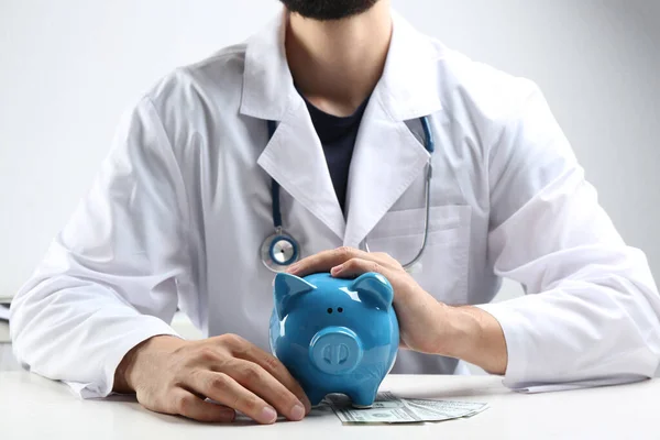 Doutor com banco de trens e dinheiro na mesa branca dentro de casa, close-up. Conceito de seguro médico — Fotografia de Stock