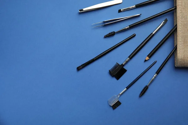 Set of professional eyebrow tools on blue background, flat lay. Space for text