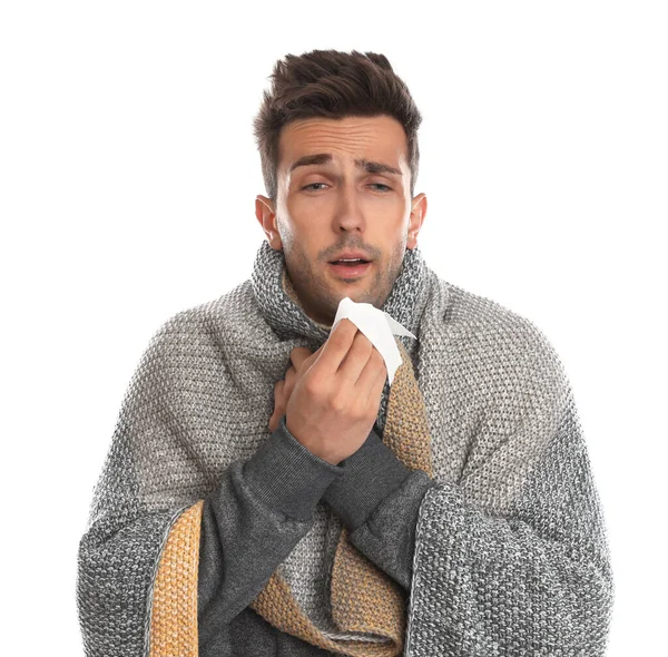 Молодой человек завернутый в теплое одеяло страдает от холода на белом фоне — стоковое фото