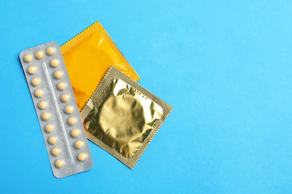 Condoms and birth control pills on light blue background, flat lay with space for text. Safe sex concept