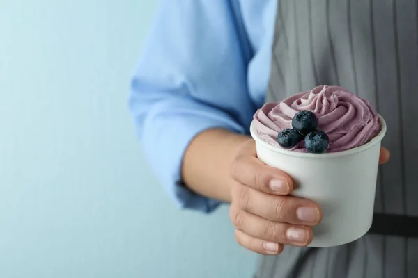 Mujer sosteniendo taza con sabroso yogur helado sobre fondo azul, primer plano — Foto de Stock