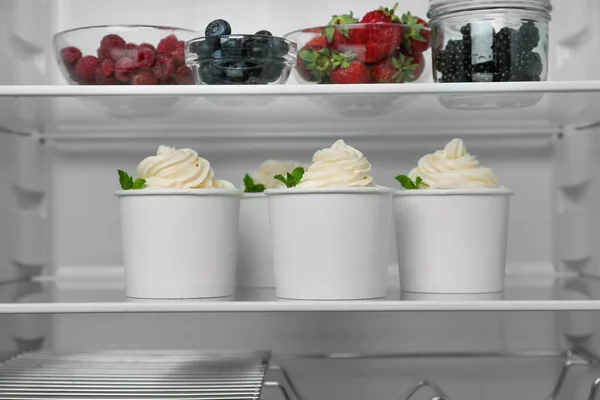 Cups with tasty frozen yogurt on fridge shelf