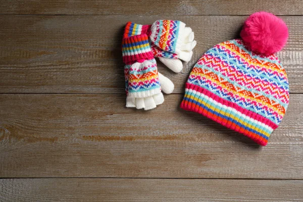 Warm knitted hat and mittens on wooden background, flat lay. Space for text