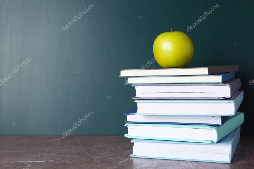 Books and apple on grey table near chalkboard, space for text. School education