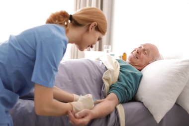 Hemşire yatakta kapalı yaşlı adama enjeksiyon yapıyor. Tıbbi yardım