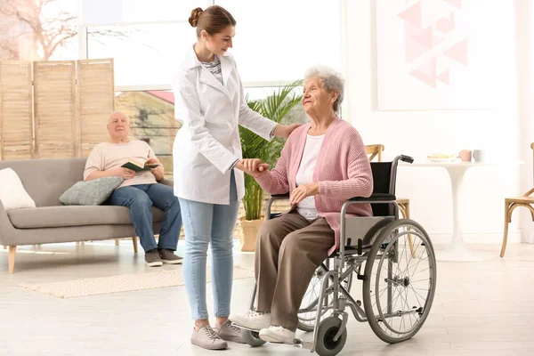 Infirmière aidant femme âgée en fauteuil roulant à l'intérieur — Photo