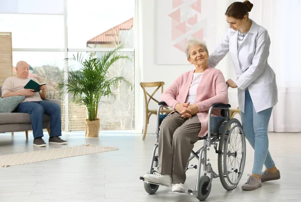 Enfermera asistiendo a anciana en silla de ruedas en interiores — Foto de Stock
