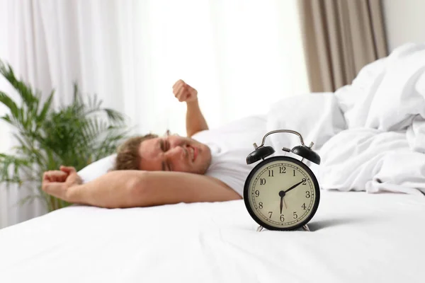 Alarm klok en wazig slaperig man op achtergrond, ruimte voor tekst. Bedtime — Stockfoto