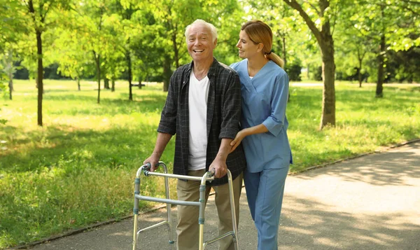 Ευτυχισμένος νοσοκόμα βοηθώντας ηλικιωμένο άνθρωπο με το περπάτημα πλαίσιο στο πάρκο — Φωτογραφία Αρχείου