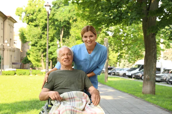 Ευτυχισμένος νοσοκόμα βοηθώντας τον ηλικιωμένο άνθρωπο σε αναπηρικό αμαξίδιο στο πάρκο — Φωτογραφία Αρχείου