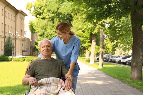 Szczęśliwy pielęgniarka pomoc starszy mężczyzna w Wheelchair w Park — Zdjęcie stockowe