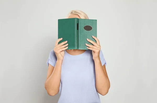 Mature woman reading book on light background — Stock Photo, Image