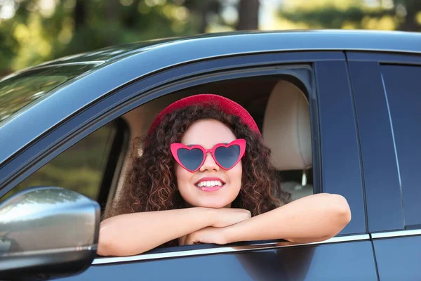 Νέα όμορφη Αφροαμερικάνα γυναίκα φορώντας καρδιά σε σχήμα γυαλιά στο αυτοκίνητο — Φωτογραφία Αρχείου