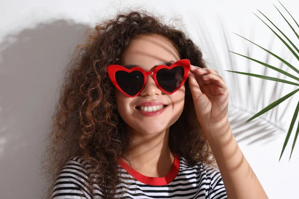 Joven hermosa mujer afroamericana con gafas en forma de corazón y hoja de palma tropical sobre fondo blanco —  Fotos de Stock
