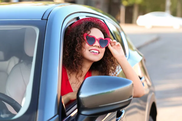 Jovem bela mulher afro-americana usando óculos em forma de coração no carro — Fotografia de Stock