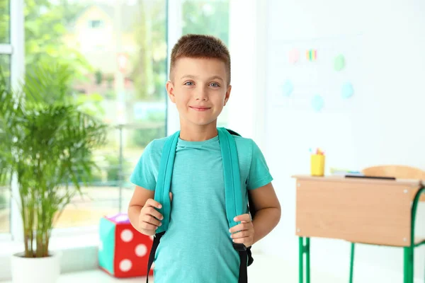 Lindo niño pequeño con mochila en el aula en la escuela —  Fotos de Stock