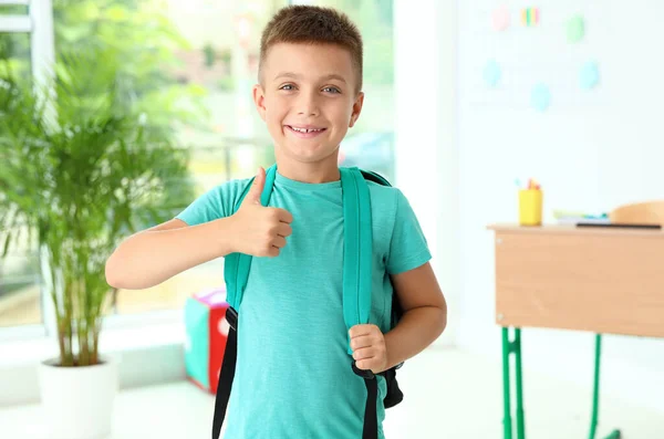 가방을 들고 교실에서 엄지 손가락들을 보여 주는 귀여운 남자 아이 — 스톡 사진