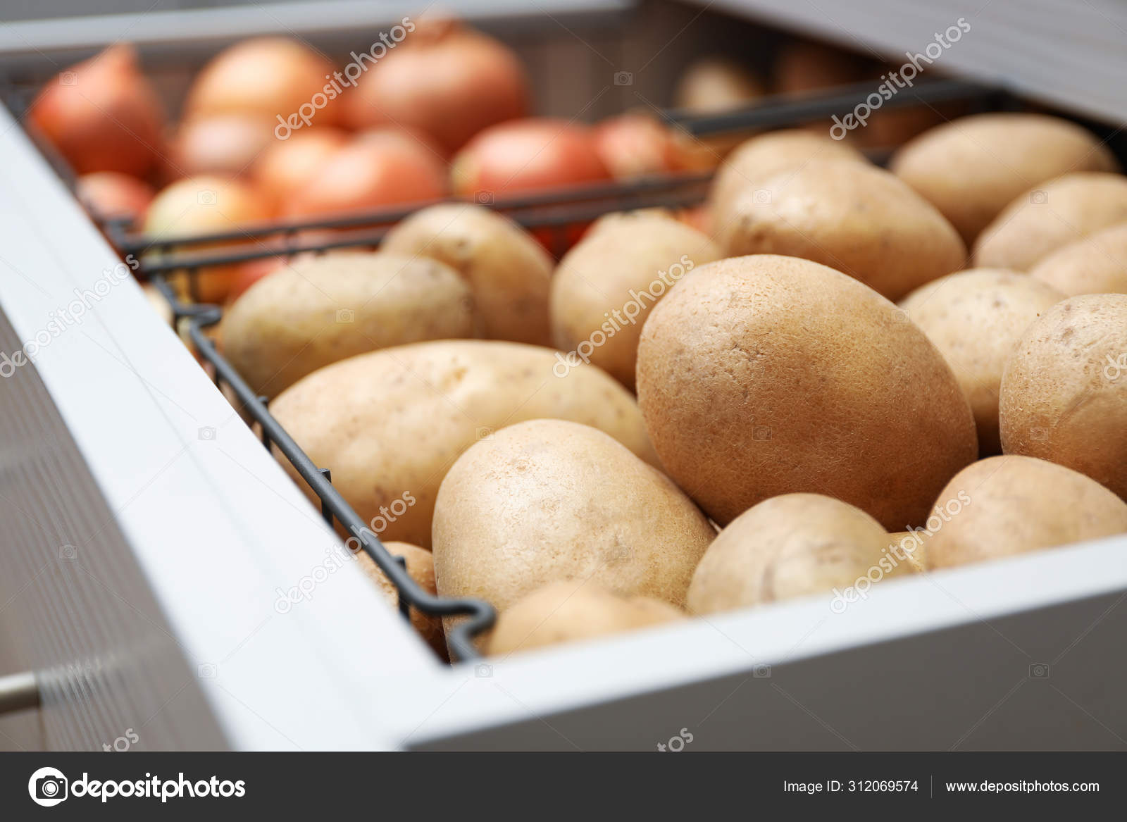 Open drawer with potatoes and onions, closeup. Orderly storage Stock