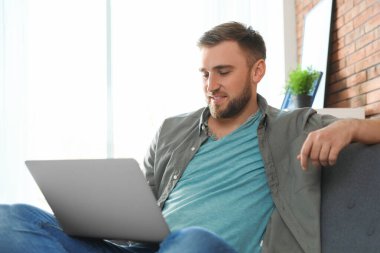 Genç adam oturma odasında dizüstü bilgisayar kullanıyor.