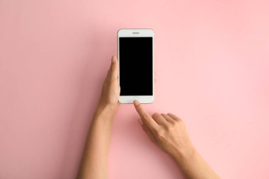 Pembe arka planda modern bir telefon tutan kadın, üst tegörüş. Metin için alan