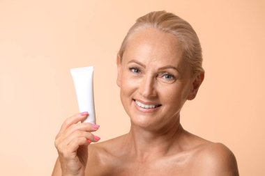 Güzel, olgun bir kadının portresi. Bej arka planda mükemmel bir cilt kremi tutuyor.