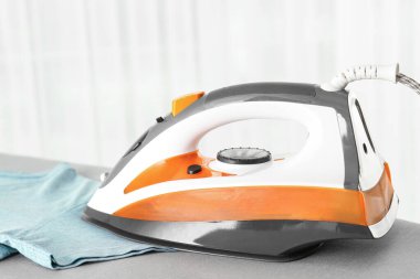 Modern elektrikli ütü ve temiz tişört arka planda ışığa karşı, yakın plan