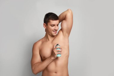 Işık arka planda koltuk altı için deodorant uygulayan genç adam