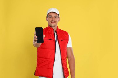 Sarı arka planda cep telefonu olan mutlu genç kurye