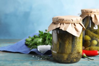 Mavi ahşap masada salatalık turşulu kavanozlar, metin için yer.