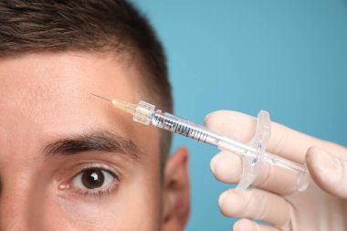 Açık mavi arka planda yüz enjeksiyonu yaptıran adam, yakın plan. Estetik ameliyat