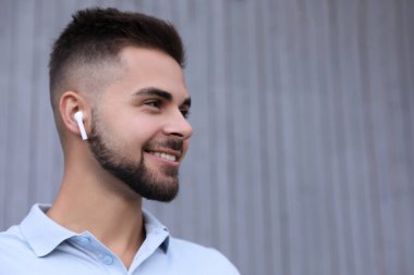 Gri duvarın yanında müzik dinleyen kablosuz kulaklıklı genç bir adam. Metin için boşluk