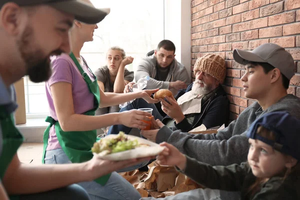 Volunteers giving food to poor people indoors — Stock Photo, Image