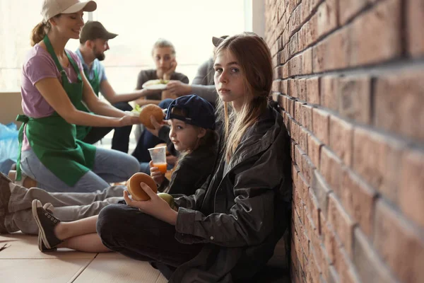 Дівчина-підліток з іншими бідними людьми отримує їжу від волонтерів у приміщенні — стокове фото