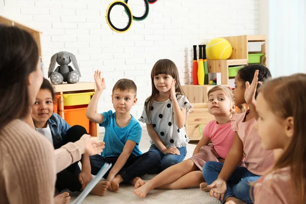 Kindergarten teacher reading book to cute little children indoors — Stock Photo, Image