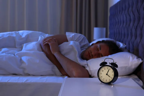 Väckarklocka på nattduksbord nära sovande ung man. Sänggåendet — Stockfoto
