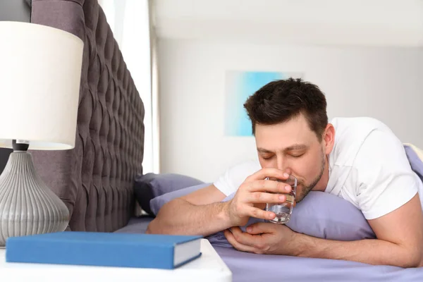 英俊的男人躺在枕头上喝水。 该睡觉了 — 图库照片