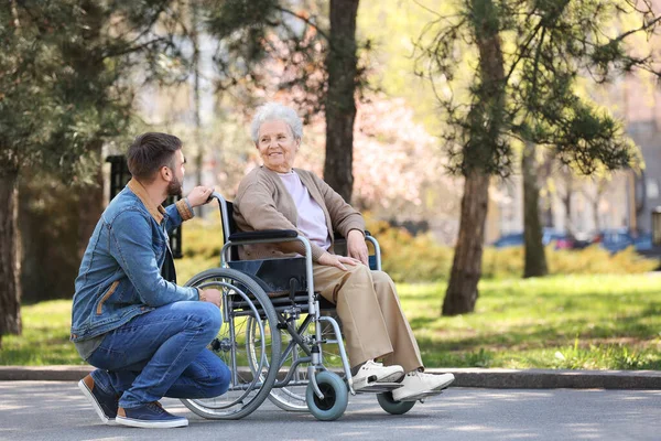 Park 'ta genç bir adamla tekerlekli sandalyede oturan yaşlı kadın. — Stok fotoğraf