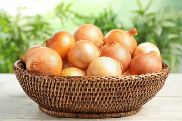 Weidenkorb mit reifen Zwiebeln auf weißem Holztisch vor verschwommenem Hintergrund — Stockfoto