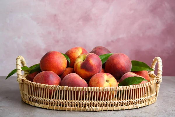 Wicker tray with tasty peaches on grey table against pink background — Stock Photo, Image