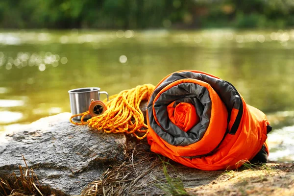 Rolled sleeping bag and other camping gear near lake