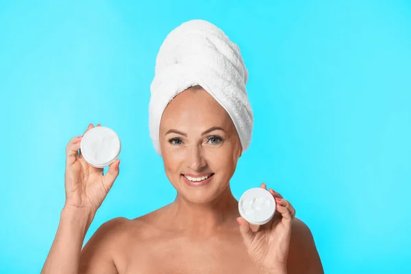 Portrait of beautiful mature woman with perfect skin holding jars of cream on light blue background — Stock Photo, Image