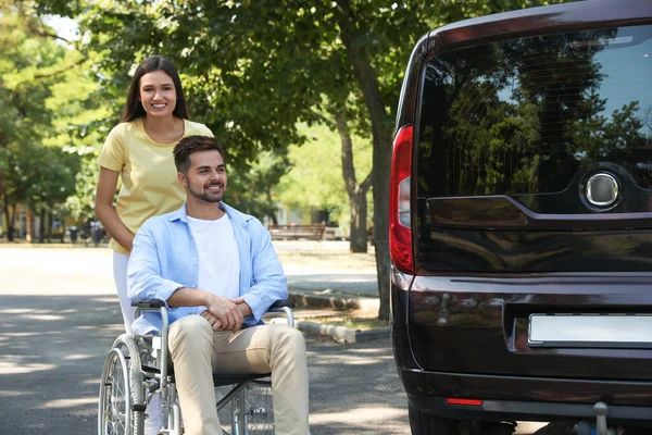 Young woman with man in wheelchair near van outdoors — Stock Photo, Image