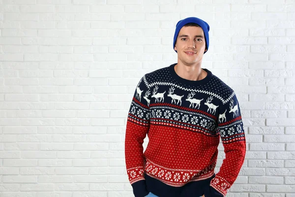 Portrait of young man in Christmas sweater and hat near white brick wall. Space for text — Stock Photo, Image