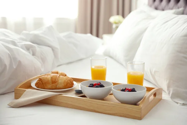 Bricka med god frukost på sängen i ljust rum — Stockfoto