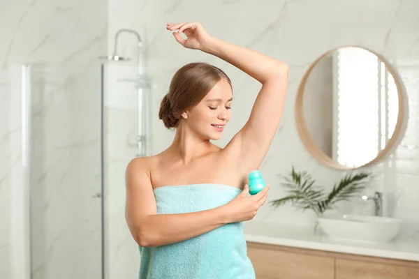 Young woman applying fresh roll-on deodorant to armpit in bathroom — Stock Photo, Image