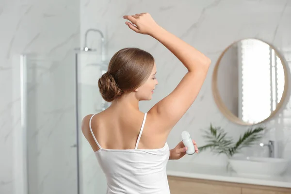 Jonge vrouw aanbrengen van verse roll-on deodorant op oksel in de badkamer — Stockfoto